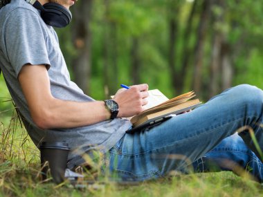 Genç bir öğrenci kitap okuyor ve sınavlara hazırlanıyor. Parktaki çimlerin üzerinde oturuyor..