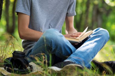 Genç bir öğrenci kitap okuyor ve sınavlara hazırlanıyor. Parktaki çimlerin üzerinde oturuyor..