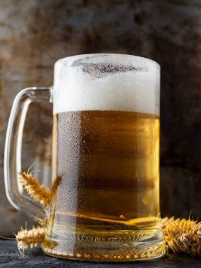 Paslı arka planda bir kupa bira ve buğday kulağı. Bir bardak soğuk biranın yakın çekimi.