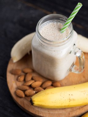 Kavanozdaki ahşap masada taze muz suyu. Yulaf ezmesi ve bademle