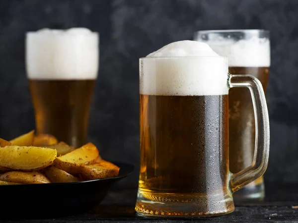 Three glasses of light beer and country potatoes on a dark table