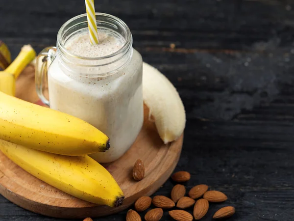 Kavanozdaki ahşap masada taze muz suyu. Yulaf ezmesi ve bademle