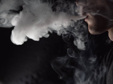 Erkek bir vampir avcısının karanlık bir arka planda buhar bulutu üflemesi.