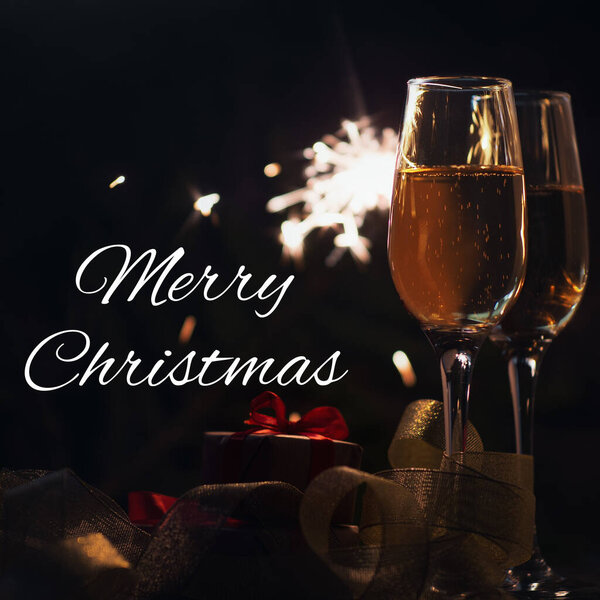 Merry Christmas text and two glasses of champagne dark background