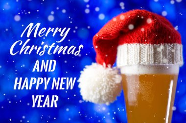 - Mutlu Noeller. Bir bardak bira ve IPA Noel Baba şapkası şenlik arka planında mavi metin.
