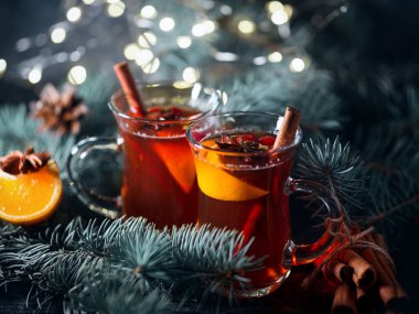 Sıcak kış alkollü kokteyl. Baharatlı ve mandallı şarap. Mavi ladin dallı, karanlık bir masada.