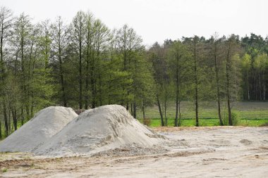 Genç yapraklı ağaçların arka planına karşı iki yığın inşaat kumu. İnşaat çalışmaları bu bölgede planlanıyor.