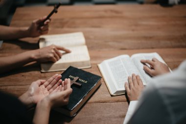 Bir grup Hıristiyan birlikte oturup odalarında açık İncil sayfaları olan ahşap bir masanın etrafında dua ediyorlar. Allah 'ın lütuf ve ihsanını dileyin.