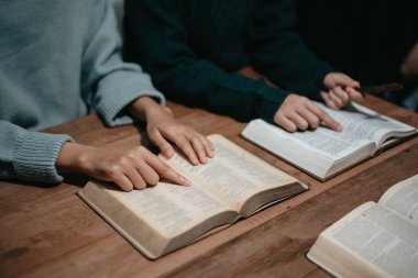 Bir grup Hıristiyan birlikte oturup odalarında açık İncil sayfaları olan ahşap bir masanın etrafında dua ediyorlar. Allah 'ın lütuf ve ihsanını dileyin.