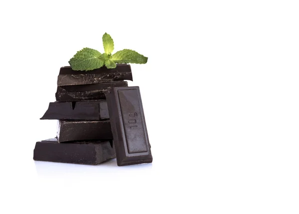 Resimdeki siyah çikolata, nane yaprağı olan birkaç tablet var, parlak bir yüzeye vardır. Arkasında beyaz bir arka planı vardır.