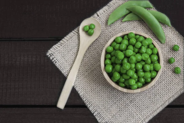 Ahşap kase bezelye ile bir tahta kaşık ve bazı pods bezelye, ahşap bir tahta üzerinde etrafında var. Yatay biçimde.