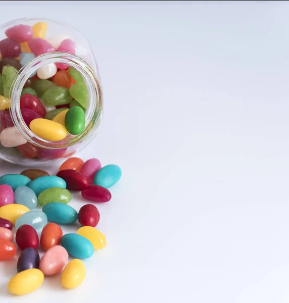 Beyaz arka plan üzerinde dağınık renkli jöle fasulye ile küçük cam kavanoz. Yatay biçimde.