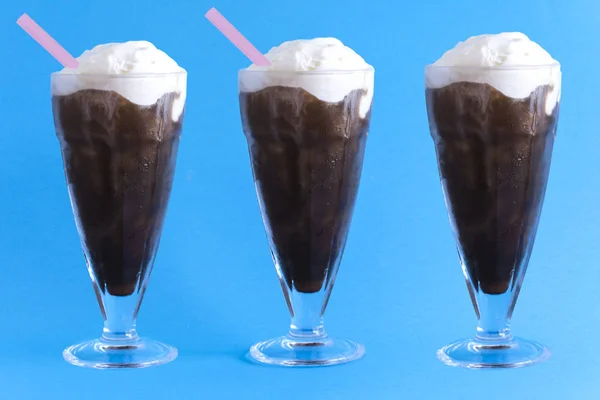 Üç bardak kahve rüşvet ile krem dondurma, orta cam pembe pipet, mavi bir arka plan üzerinde vardır. Yatay biçimde.
