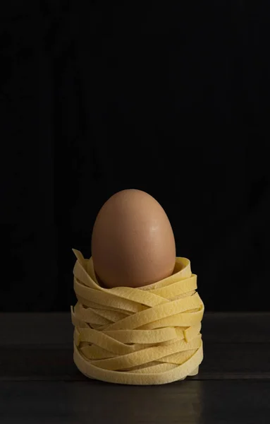 Fettuccine yumurta ile kahverengi ahşap masa, siyah bir arka plan üzerinde ham. Yatay biçimde.