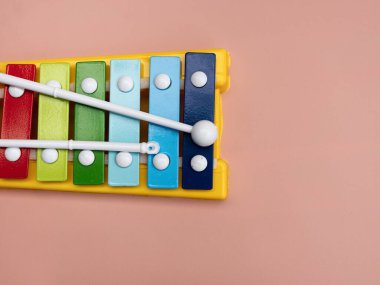 Canlı, renkli bir oyuncak ksilofonun tokmakları sade pembe arka planda duruyor. Kopya alanı da mevcut..