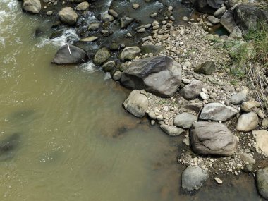 Nehir kenarındaki taşların ve kayaların çeşitli büyüklüklerinde bulanık suların aktığı sakin bir nehrin yüksek açılı görüntüsü..