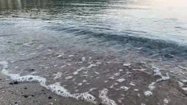 Sabah küçük deniz dalgaları sakin havada kumlu sahili yıkıyor. Yumuşak dalgalı ve köpüklü deniz manzarası, arka plan, rahatlama, meditasyon ve doğa atmosferi kavramları için mükemmel.