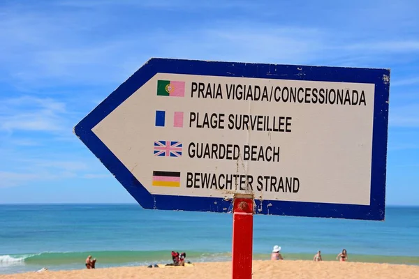 Multilingual guarded beach sign on the beach with the ocean to the rear and people enjoying the setting, Albufeira, Portugal, Europe.