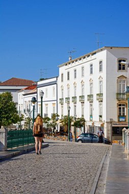 Tavira, Portekiz - 12 Haziran 2017 - Roma arasında yürüyen genç kadın arka, Tavira, Algarve, Portekiz, Avrupa'ya şehir binaları ile 12 Haziran 2017 köprü.