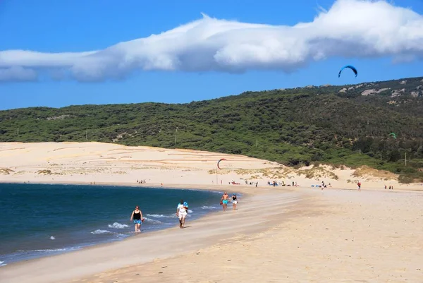 Relaxační turisté na pláži Valdevaqueros s kite surfaři dozadu, Tarifa, Španělsko. — Stock fotografie