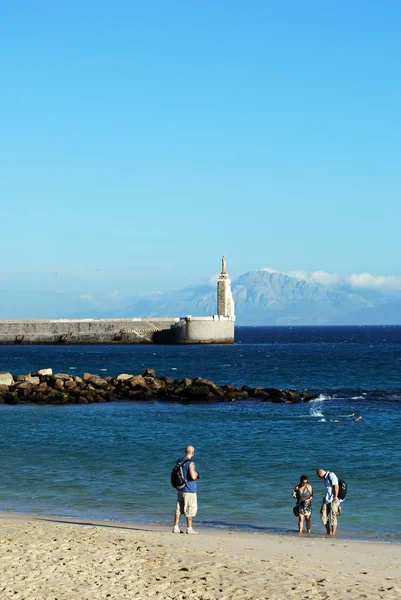 Ver Turistas en la playa con vistas a la entrada del puerto que conduce a la costa marroquí y las montañas del Rif, Tarifa, Cádiz . —  Fotos de Stock