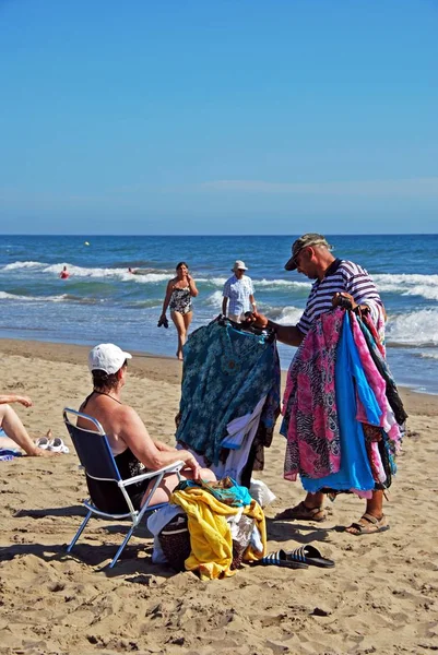 Comerciante de playa mostrando sus mercancías a un turista en la playa de la Vibora, Elviria, Marbella, España . — Foto de Stock