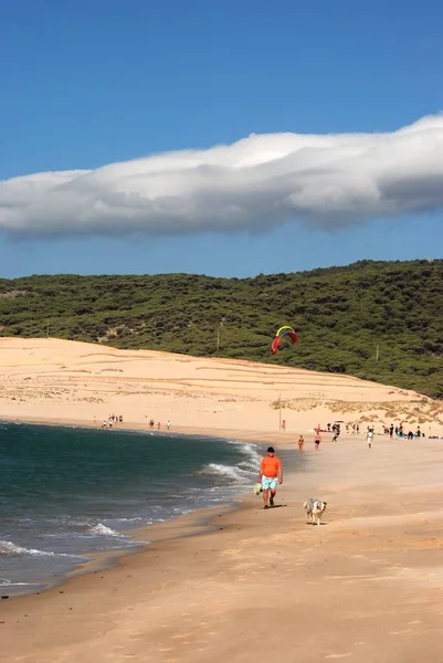 Туристы, идущие вдоль пляжа Вальдевакерос с кайтсерферами в тыл, Тарифа, Испания . — стоковое фото