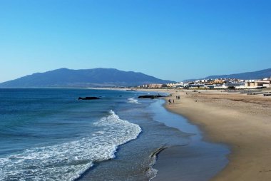 Şehir ve dağlara doğru manzaralı plajda dinlenen turistler, Tarifa, İspanya.