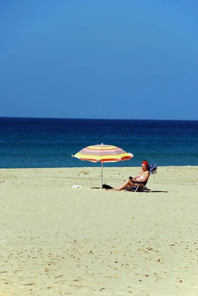 Kobieta siedząca przy parasolu na plaży czytająca magazyn, Zahara de los Atunes, Hiszpania. — Zdjęcie stockowe