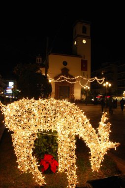 Noel'de arka kilise ile gece Anayasa Meydanı'nda Aydınlatılmış çerçeve reindeer, Fuengirola, İspanya.