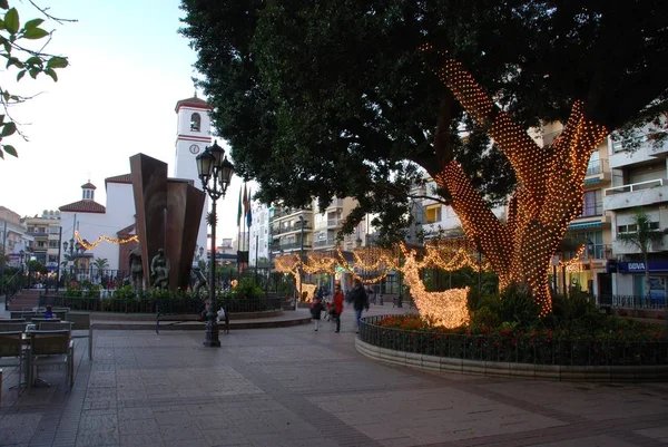 Fonte na Praça da Constituição ao anoitecer com a Igreja na retaguarda no Natal, Fuengirola, Espanha . — Fotografia de Stock