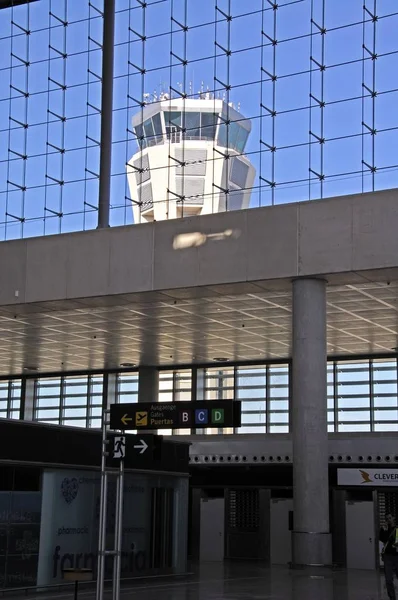 Sala de facturación en la terminal de tres salidas con la torre de control en la parte trasera vista a través de la ventana en el aeropuerto de Málaga, Málaga, España . —  Fotos de Stock