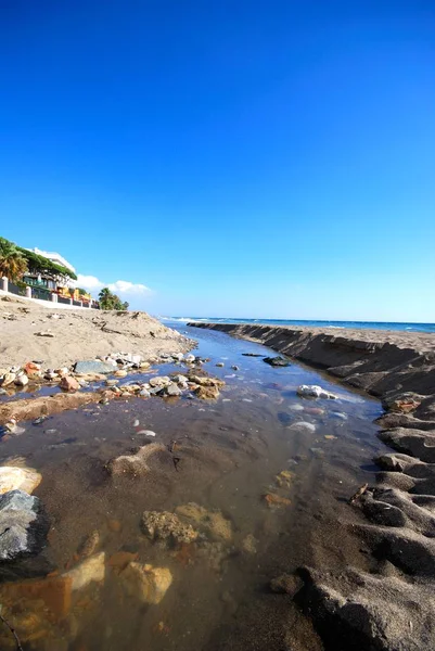 Prohlédněte si tichou pláž Daitona a pobřeží s potokem v popředí, Marbella, Španělsko. — Stock fotografie