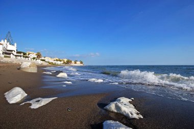 View along the beach towards apartments with large rocks along the shoreline, Sitio de Calahonda, Spain. clipart