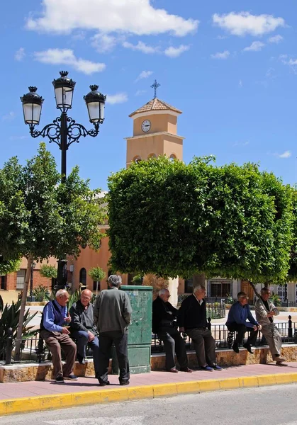 Ältere spanische Männer plaudern am Rande des Stadtplatzes mit dem Kirchturm im Hintergrund, albox, spanien. — Stockfoto