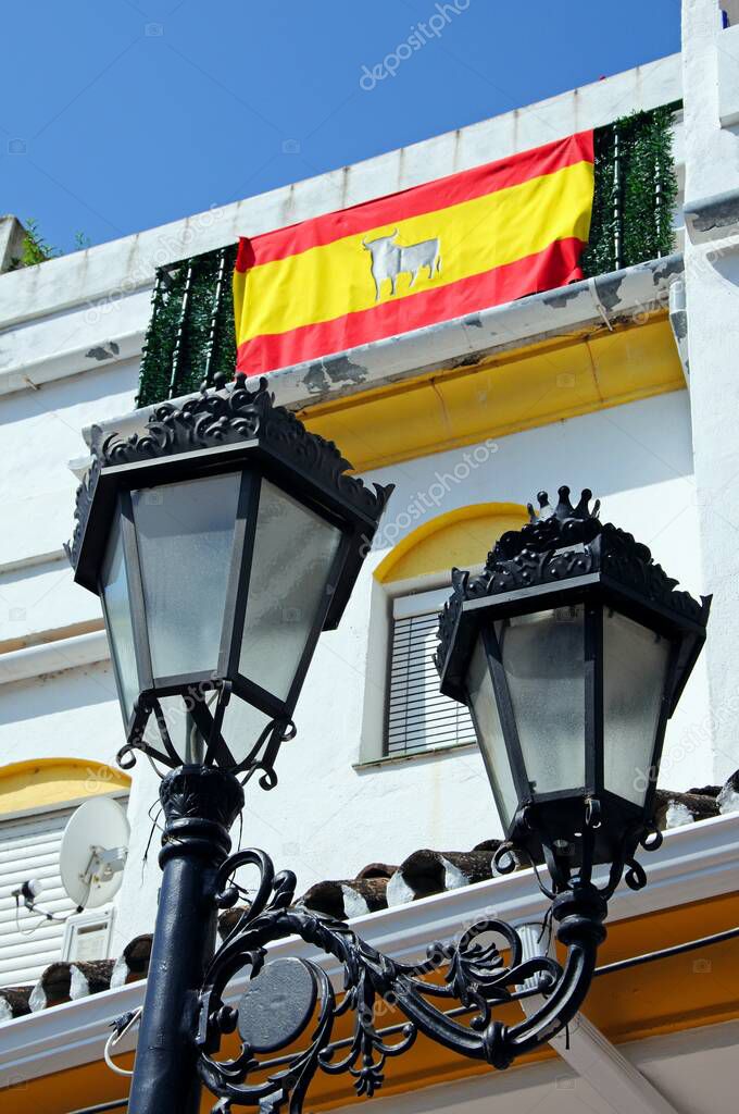 Wrought iron streetlight with a Spanish flag on townhouse balcony to the rear, Pueblo Blanco, Benahavis, Costa del Sol, Malaga Province, Andalucia, Spain, Western Europe.