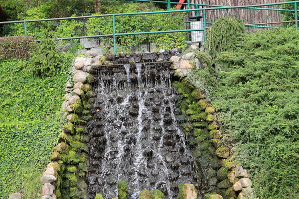 The photo shows an artificial waterfall in Gdansk Zoo, surrounded by greenery and a small pond.
