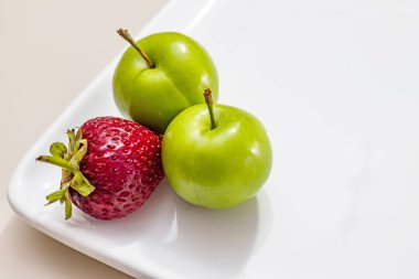 beyaz plaka çilek ile yeşil erik yakın.