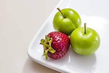 beyaz plaka çilek ile yeşil erik yakın.