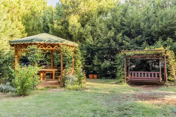 wooden pergola and swing in garden with lamp and trees.