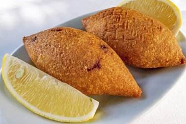 Close up Ready to eat Turkish stuffed meatballs with sliced lemons in white plate.