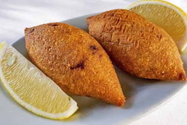 Close up Ready to eat Turkish stuffed meatballs with sliced lemons in white plate.