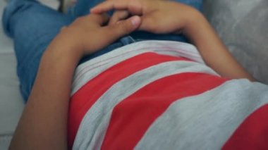 Bir çocuk kanepede yatar ve yaslanır.