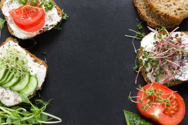 Krem peynirli, mikroyeşillikli, domatesli ve salatalıklı sağlıklı sandviçler. Sağlıklı beslenme, diyet, vejetaryen yiyecekler, sağlıklı kahvaltı. Siyah arka plan, boş şablon.