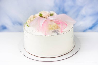 Küçük kız için vaftiz pastası, pembe kanatlı beyaz pasta, çikolata bebek figürü ve arka planda pembe güller. Vaftiz partisi çikolatası