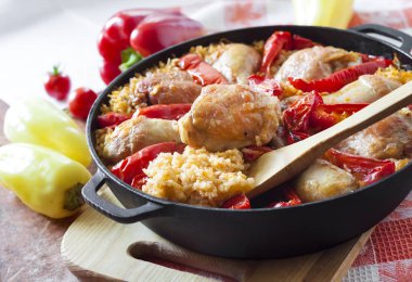 Pirinç ve dökme demir güveç içinde kırmızı dolmalık biber bir yatak üzerinde pişmiş tavuk uyluk ve bacaklar