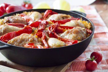 Pirinç ve dökme demir güveç içinde kırmızı dolmalık biber bir yatak üzerinde pişmiş tavuk uyluk ve bacaklar