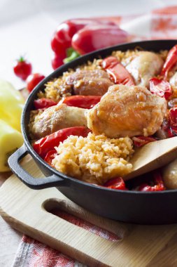 Pirinç ve dökme demir güveç içinde kırmızı dolmalık biber bir yatak üzerinde pişmiş tavuk uyluk ve bacaklar