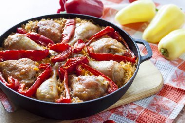 Pirinç ve dökme demir güveç içinde kırmızı dolmalık biber bir yatak üzerinde pişmiş tavuk uyluk ve bacaklar