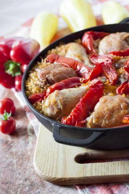 Pirinç ve dökme demir güveç içinde kırmızı dolmalık biber bir yatak üzerinde pişmiş tavuk uyluk ve bacaklar